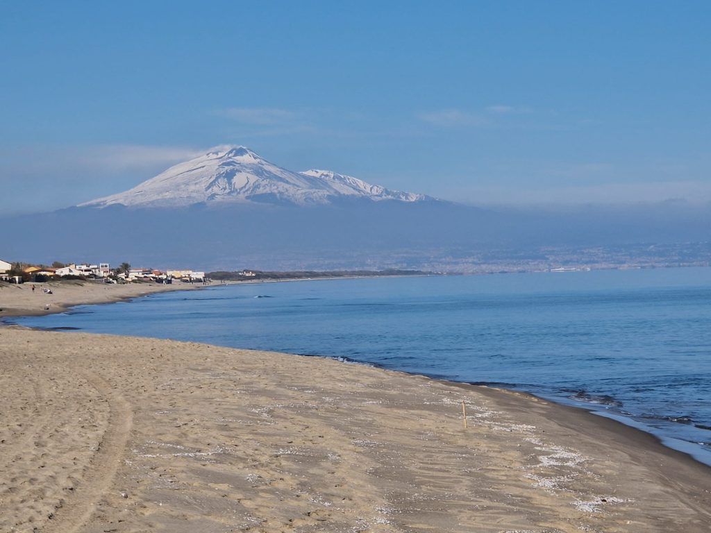 🇮🇹 Italiano Spiaggia invernale di Agnone Bagni con vista sull’Etna innevato. 🇬🇧 English Winter beach in Agnone Bagni with stunning view of snow-covered Mount Etna. 🇩🇪 Deutsch Winterlicher Strand in Agnone Bagni mit Blick auf den verschneiten Ätna. 🇫🇷 Français Plage d’hiver à Agnone Bagni face à l’Etna recouvert de neige. 🇨🇿 Čeština Zimní pláž v Agnone Bagni s výhledem na zasněženou sopku Etna. 🇧🇬 Български Зимен плаж в Аньоне Бани с изглед към заснежения връх Етна. 🇵🇱 Polski Zimowa plaża w Agnone Bagni z widokiem na ośnieżoną Etnę. 🇧🇷 Português (BR) Praia de inverno em Agnone Bagni com o vulcão Etna coberto de neve ao fundo. 🇹🇷 Türkçe Kış manzaralı Agnone Bagni sahili – arka planda karla kaplı Etna Dağı. 🇬🇷 Ελληνικά Χειμωνιάτικη παραλία στην Agnone Bagni με θέα το χιονισμένο ηφαίστειο Αίτνα. 🇵🇹 Português (PT) Praia de inverno em Agnone Bagni com vista para o Etna coberto de neve. 🇪🇸 Español Playa invernal en Agnone Bagni con el Etna nevado en el horizonte.