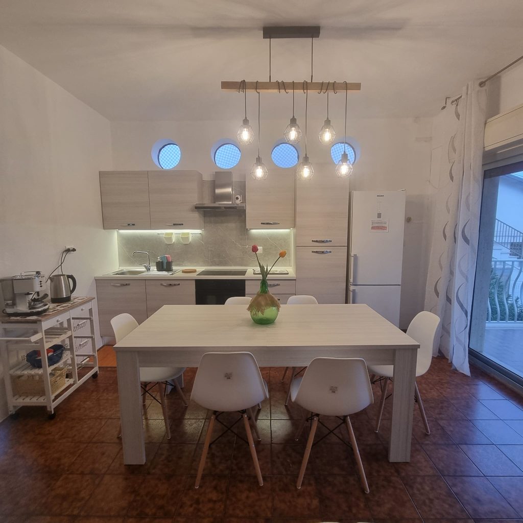 Lingua Testo 🇮🇹 IT Cucina con tavolo bianco, sedie moderne e luci a sospensione 🇬🇧 EN Kitchen with white table, modern chairs and hanging lights 🇩🇪 DE Küche mit weißem Tisch, modernen Stühlen und Hängelampen 🇫🇷 FR Cuisine avec table blanche, chaises modernes et suspensions 🇨🇿 CZ Kuchyně s bílým stolem, moderními židlemi a závěsným osvětlením 🇧🇬 BG Кухня с бяла маса, модерни столове и висящо осветление 🇵🇱 PL Kuchnia z białym stołem, nowoczesnymi krzesłami i lampami wiszącymi 🇧🇪 NL Keuken met witte tafel, moderne stoelen en hanglampen 🇹🇷 TR Beyaz masa, modern sandalyeler ve sarkıt lambalı mutfak 🇬🇷 GR Κουζίνα με λευκό τραπέζι, μοντέρνες καρέκλες και κρεμαστά φώτα 🇵🇹 PT Cozinha com mesa branca, cadeiras modernas e luzes suspensas 🇪🇸 ES Cocina con mesa blanca, sillas modernas y lámparas colgantes