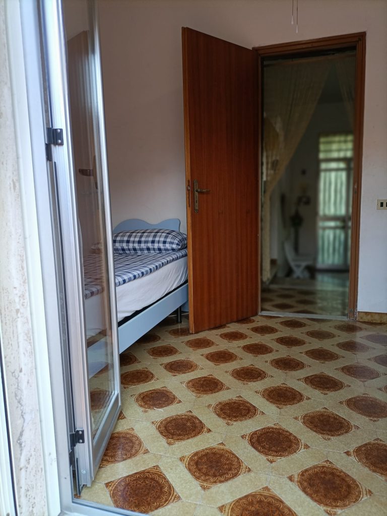 🇮🇹 IT Stanza con lettino singolo lato sinistro e porta aperta sul corridoio 🇬🇧 EN Room with single bed on the left and open door to corridor 🇩🇪 DE Zimmer mit Einzelbett links und offener Tür zum Flur 🇫🇷 FR Chambre avec lit simple à gauche et porte ouverte sur le couloir 🇨🇿 CZ Pokoj s jednolůžkem vlevo a otevřenými dveřmi do chodby 🇧🇬 BG Стая с единично легло отляво и отворена врата към коридора 🇵🇱 PL Pokój z pojedynczym łóżkiem po lewej i drzwiami do korytarza 🇧🇪 NL Kamer met eenpersoonsbed links en open deur naar gang 🇹🇷 TR Sol tarafta yatak bulunan oda ve açık koridor kapısı 🇬🇷 GR Δωμάτιο με μονό κρεβάτι αριστερά και πόρτα προς τον διάδρομο 🇵🇹 PT Quarto com cama individual à esquerda e porta aberta para o corredor 🇪🇸 ES Dormitorio con cama individual a la izquierda y puerta al pasillo